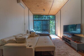 Una sala de estar moderna con un ventanal grande, un sofá, un televisor y techo de madera.