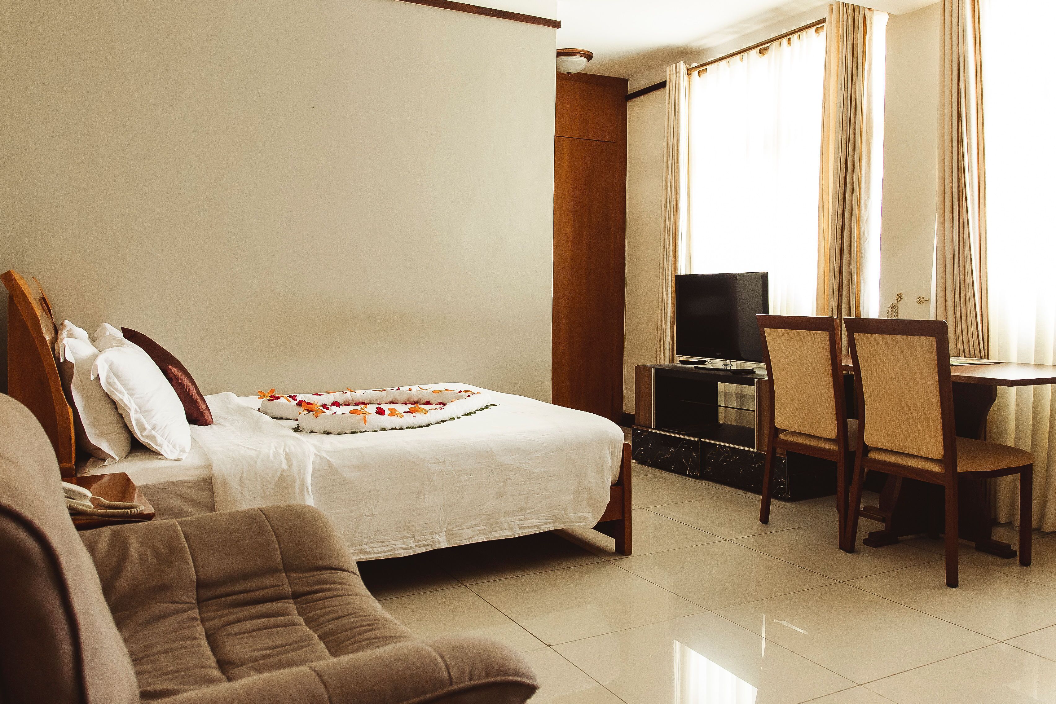 A hotel room with a bed, a TV, a dining table with chairs, and a sofa.