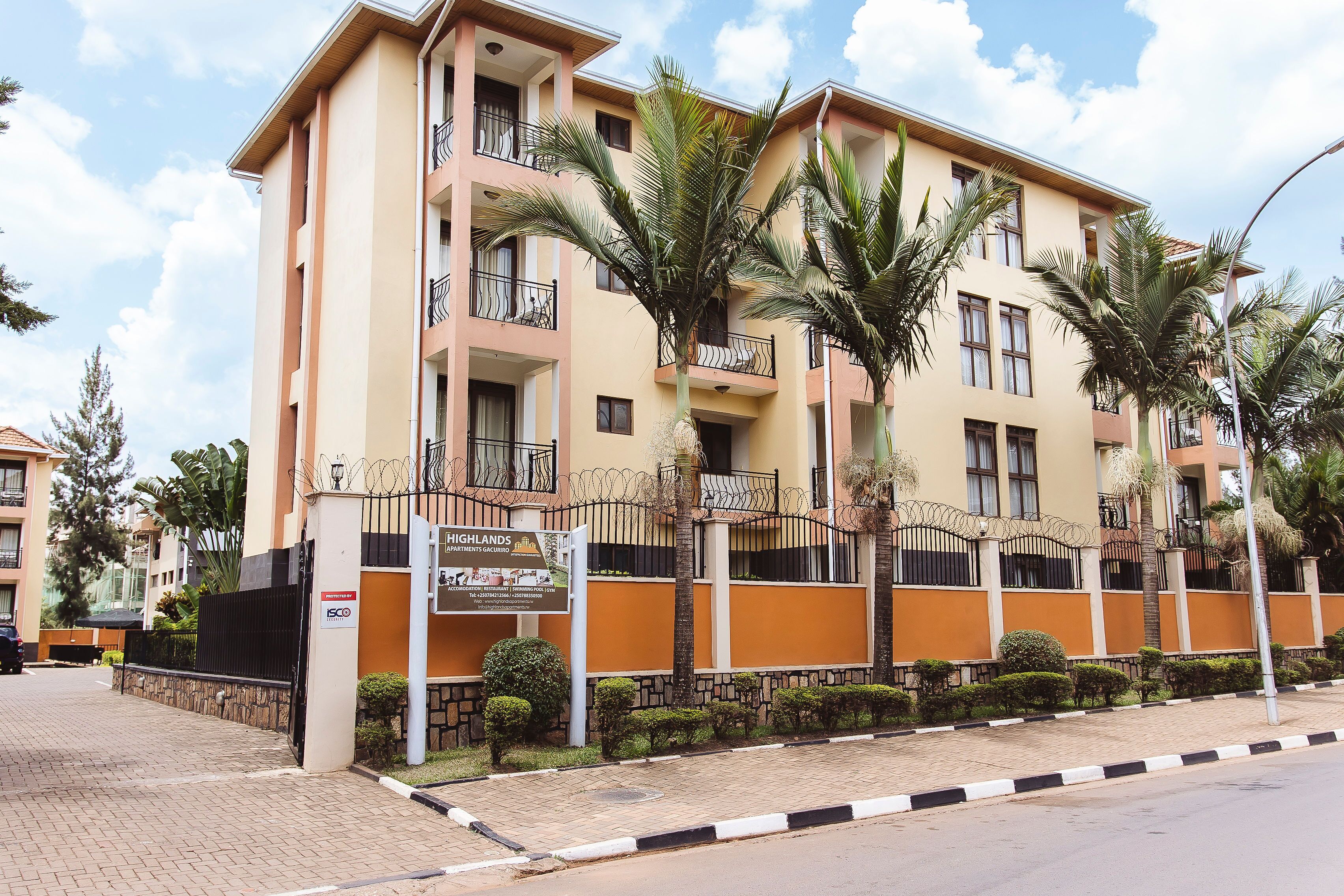 A multi-story residential building with balconies, palm trees, and a paved entrance.
