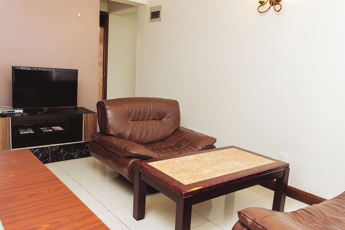 A living room with a brown leather sofa, a wooden coffee table, and a TV on a stand.