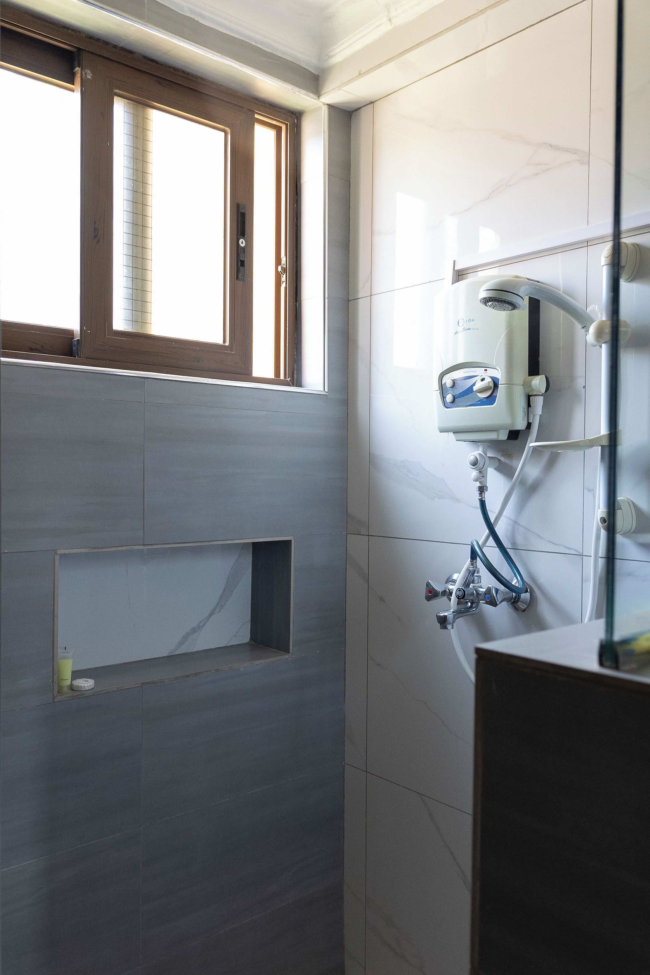 A bathroom with a window, a built-in shelf, and a shower system.