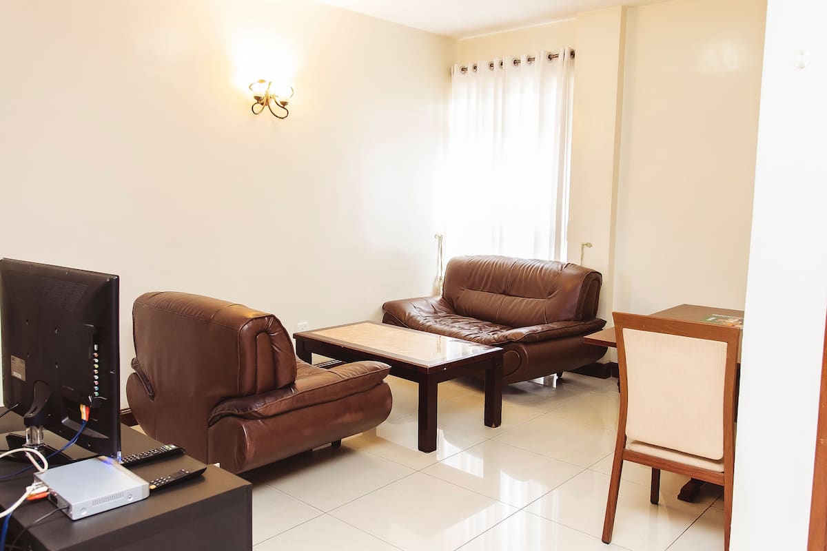 A living room with a brown leather sofa, a wooden coffee table, a TV, and a remote control.