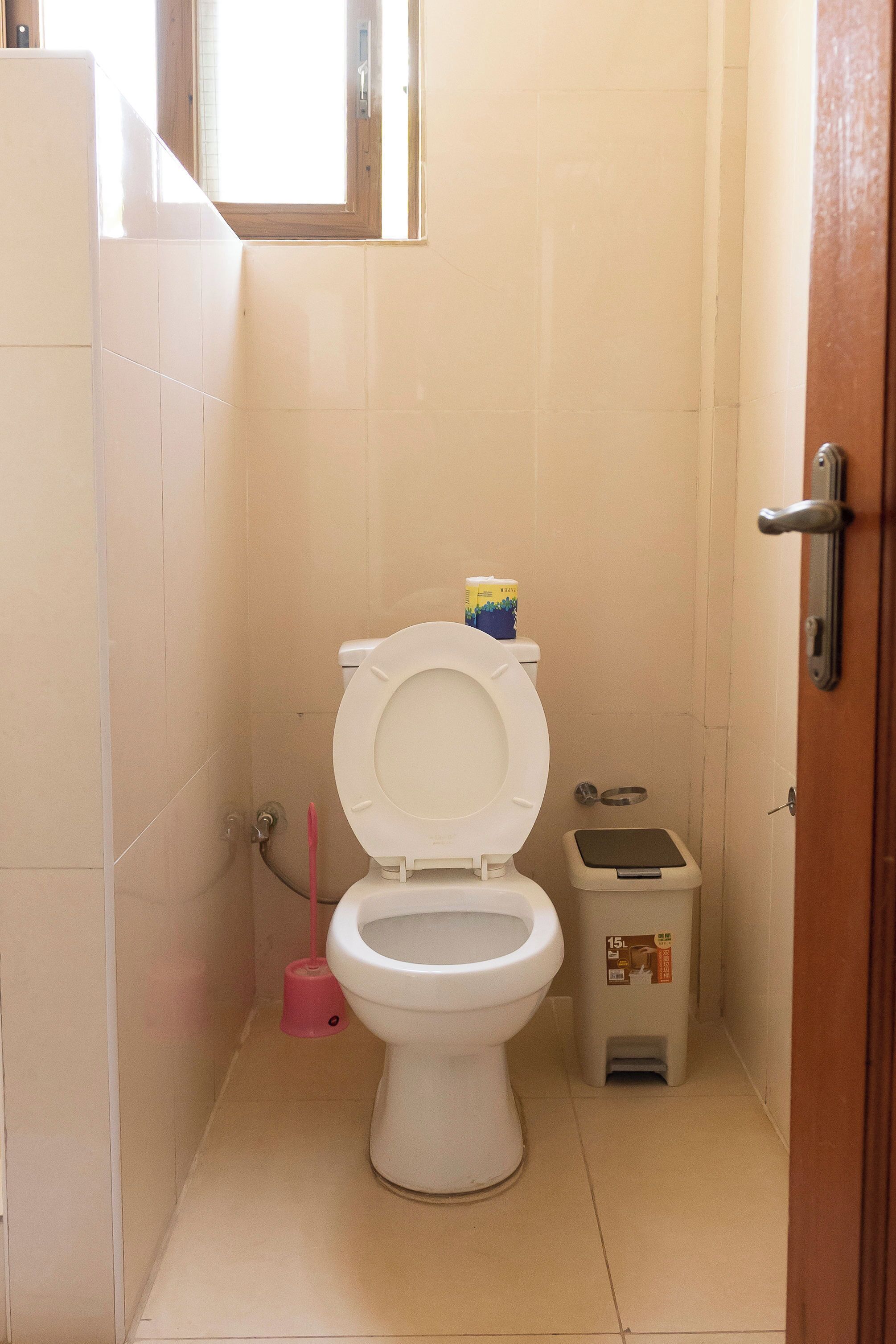A small, clean bathroom with a toilet, a trash bin, and a window.