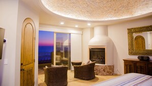 A bedroom with a fireplace, wicker chairs, a bed, and a view of the sea. - Bella Sirena A701 Penthouse Amazing Ocean Views (Puerto Peñasco)