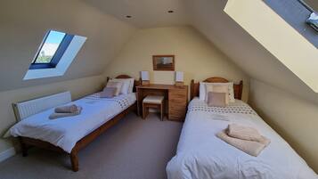 Une petite chambre bien éclairée, avec deux lits simples, un bureau et une chaise.