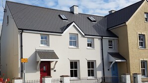 A two-story building with a red door, multiple windows, and a grey roof.