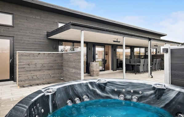 A modern outdoor hot tub area with a covered patio, a wooden fence, and a view of the backyard.