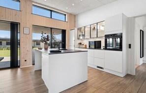 Une cuisine moderne dotée d’un îlot central, d’appareils électroménagers intégrés et de grandes fenêtres.