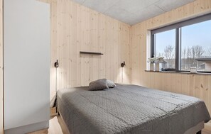 Un dormitorio con cama, paredes de madera, una ventana y una mesita de noche.