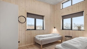 Un dormitorio con dos camas, paredes de madera y ventanas amplias con vistas al exterior.