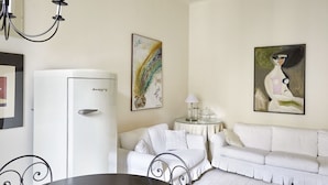 A room with a white sofa, a dining table, a white refrigerator, and two paintings on the wall. - Easylife - Jewel of art in Arco della Pace area (Milano)