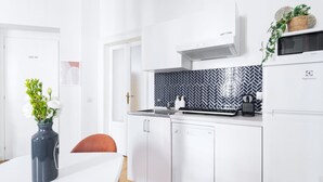 Une cuisine moderne avec des meubles blancs, un dosseret en mosaïque noire et blanche et un micro-ondes placé sur le dessus du réfrigérateur.