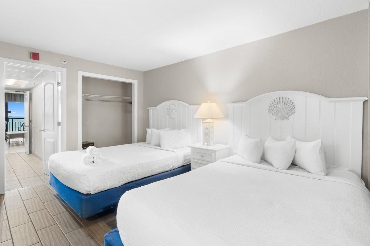 A hotel room with two beds, a walk-in closet, and a view of the beach.
