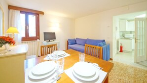 A dining area with a wooden table set for four, a television on a small table, and a blue sofa in the background. - DolceVita Apartments N. 465 (Venice)