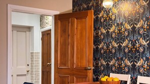 Una habitación con puerta de madera, papel tapiz estampado, una mesa con frutero y un sofá azul.