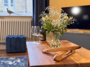 A wooden table with a vase of flowers, a bottle, and a pair of tongs. - Captivating 3-bed Cottage in Saltaire (Shipley)