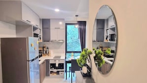 Une cuisine moderne équipée d’un four encastré, d’un réfrigérateur et d’un évier. Une fenêtre offre une vue sur les arbres et un miroir est accroché au mur.