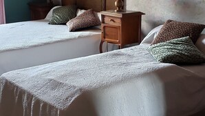Une chambre d’hôtel avec deux lits, une tête de lit en bois, une table de chevet avec une lampe et un papier peint à motifs floraux.