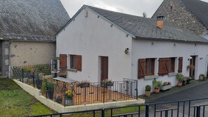 Un bâtiment blanc avec un toit en pente, des volets en bois et un petit porche agrémenté de plantes en pot.