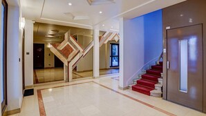 A spacious hallway with a marble floor, a red carpeted staircase, and a modern elevator. - Bright Etoile /  Bright 2 bed close to Eiffel Tower Arc the Triomphe et Champs E (Paris)