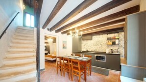 A staircase leading to a dining area with a table set for four, a kitchen with modern appliances, and exposed wooden beams on the ceiling.