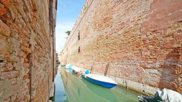 A narrow canal with boats docked along the sides, surrounded by old brick walls.