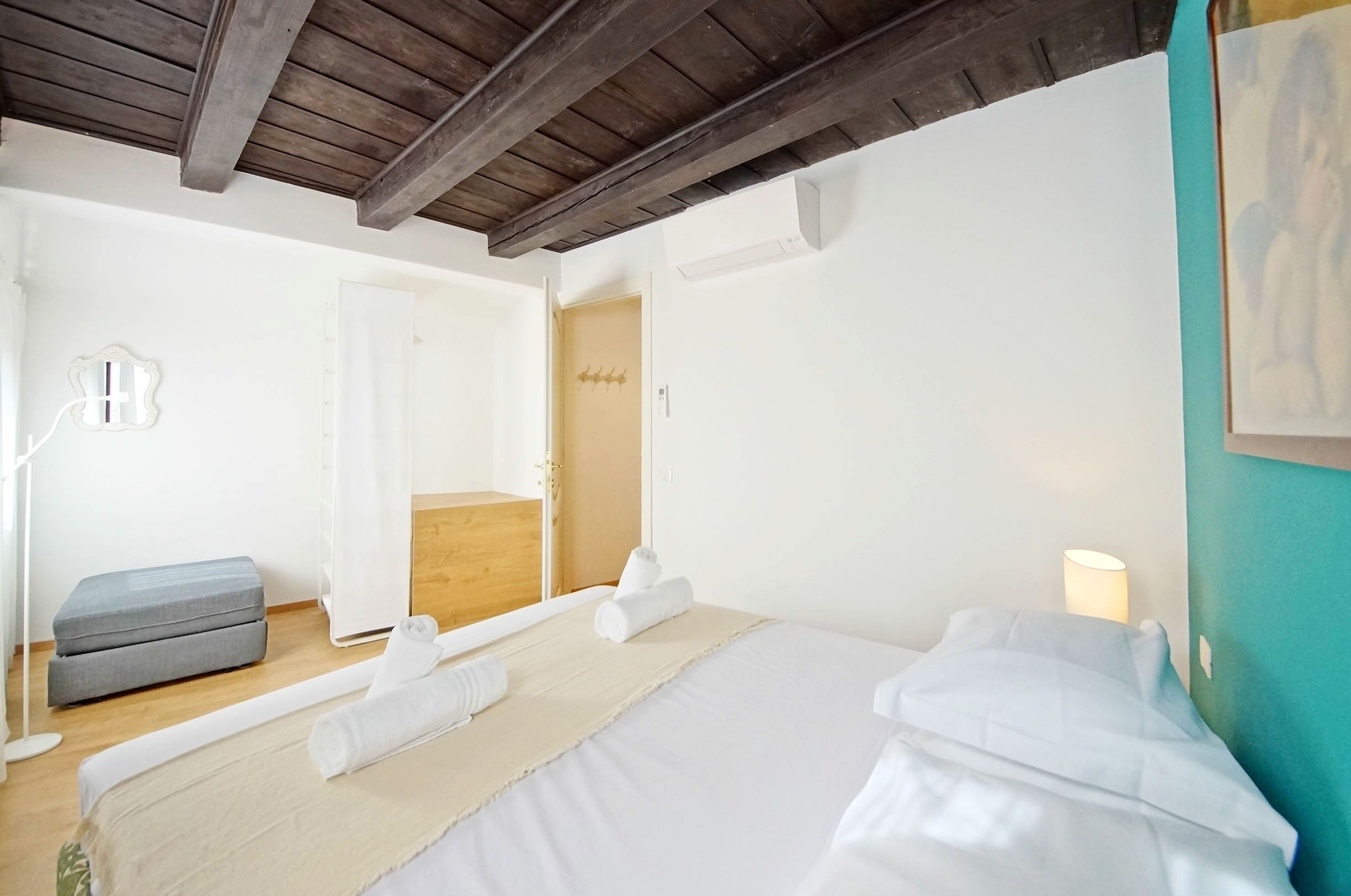 Ein Schlafzimmer mit einem Bett, einer Bank, einem Spiegel und einer Tür zu einem anderen Raum.