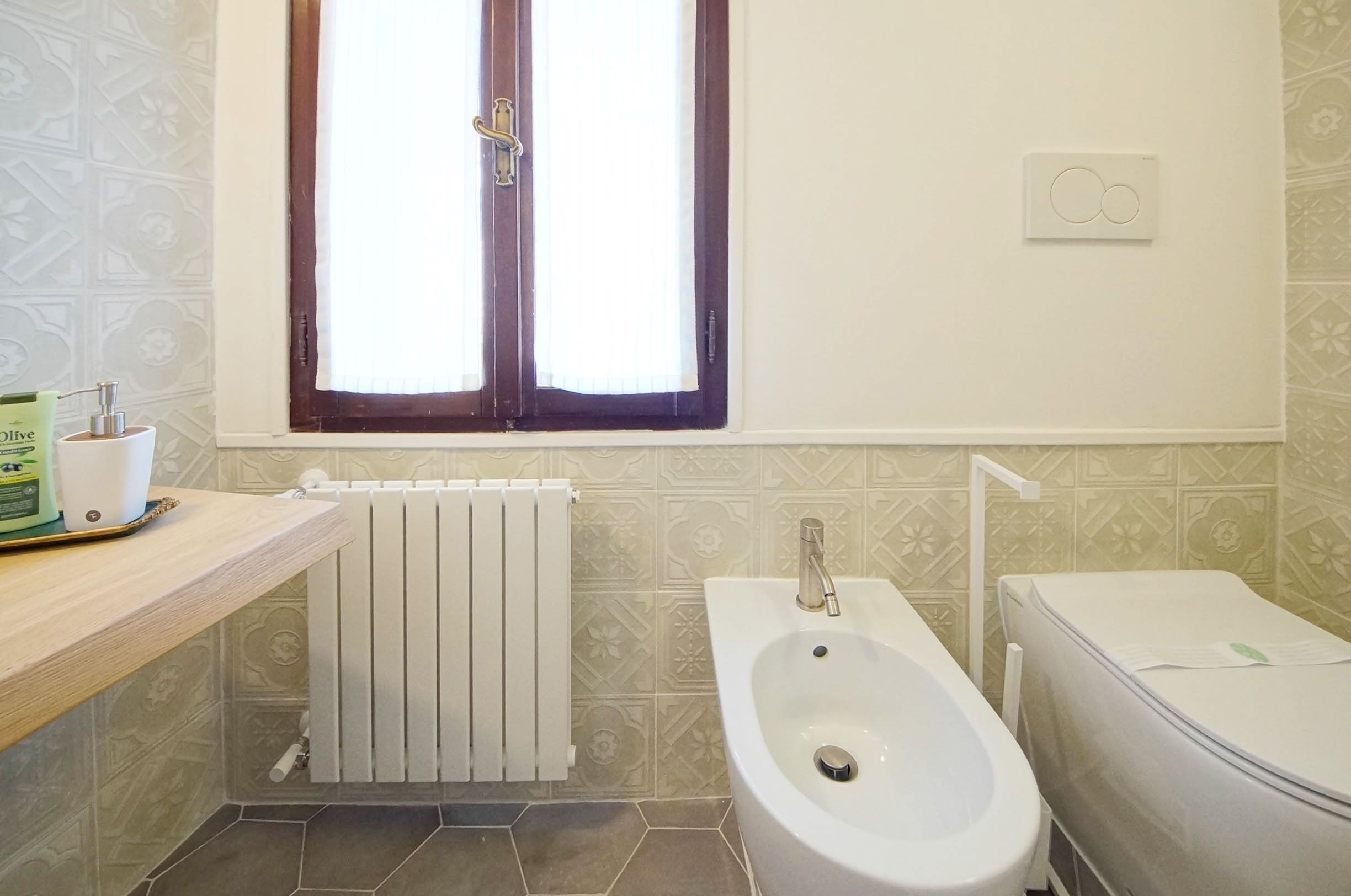 A bathroom with a bathtub, toilet, and a window with blinds.