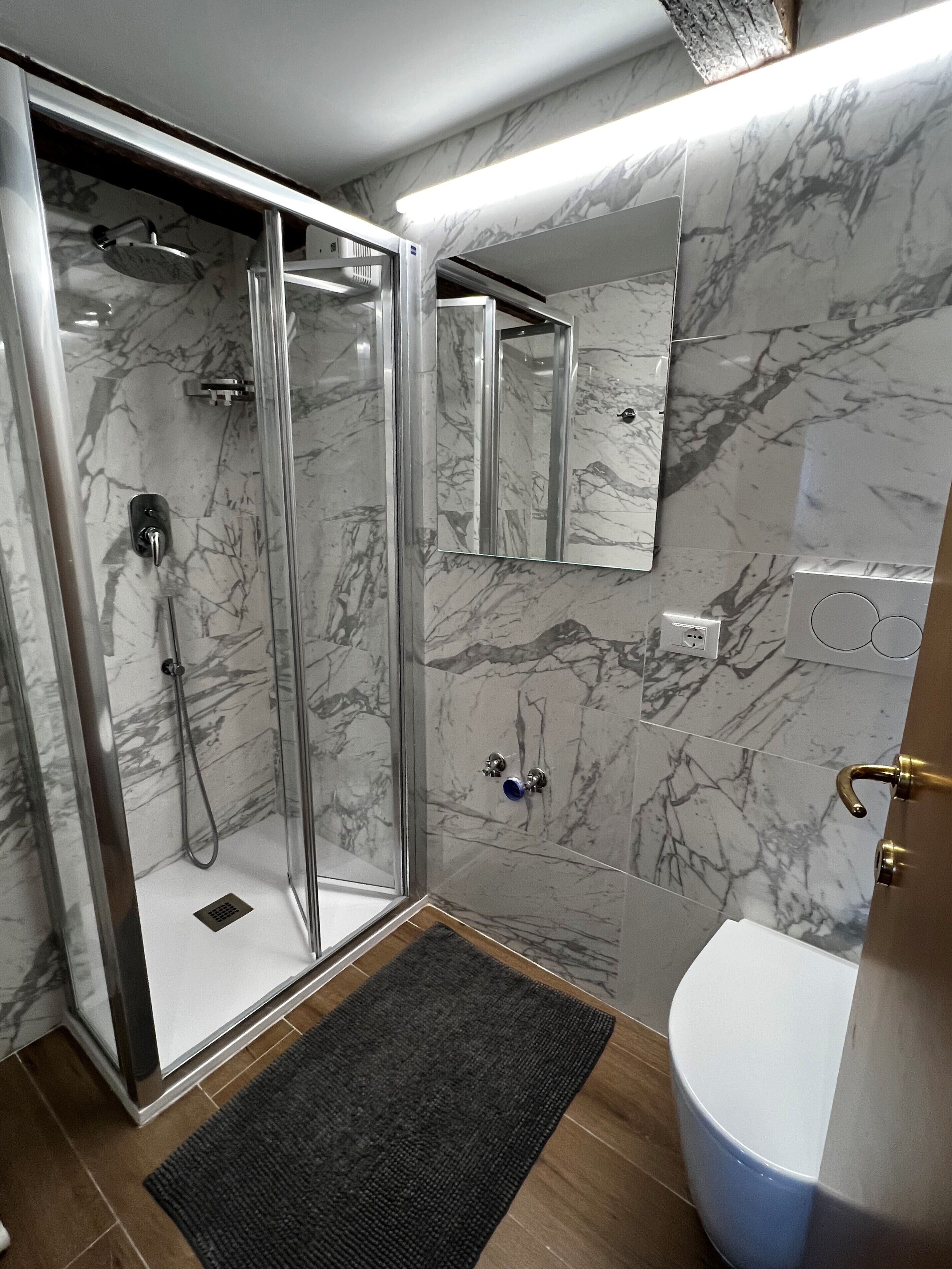 Ein Badezimmer mit einer gläsernen Duschkabine, einer weißen Toilette und einer Wand mit Marmorfliesen.