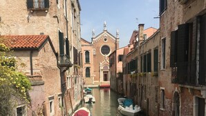 Um canal estreito com barcos atracados em ambas as margens, ladeado por edifícios históricos com fachadas de tijolo e janelas venezianas tradicionais.