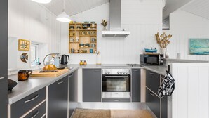 Une cuisine compacte équipée d’un four Bosch, d’un four à micro-ondes et d’un évier. On y trouve une étagère en bois avec divers ustensiles de cuisine et une petite décoration représentant un bateau.