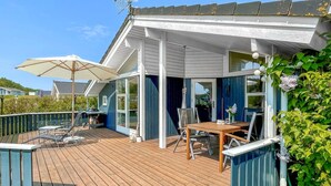 Une terrasse extérieure couverte, dotée d’une table et de chaises, d’un grand parasol et offrant une vue sur les environs.