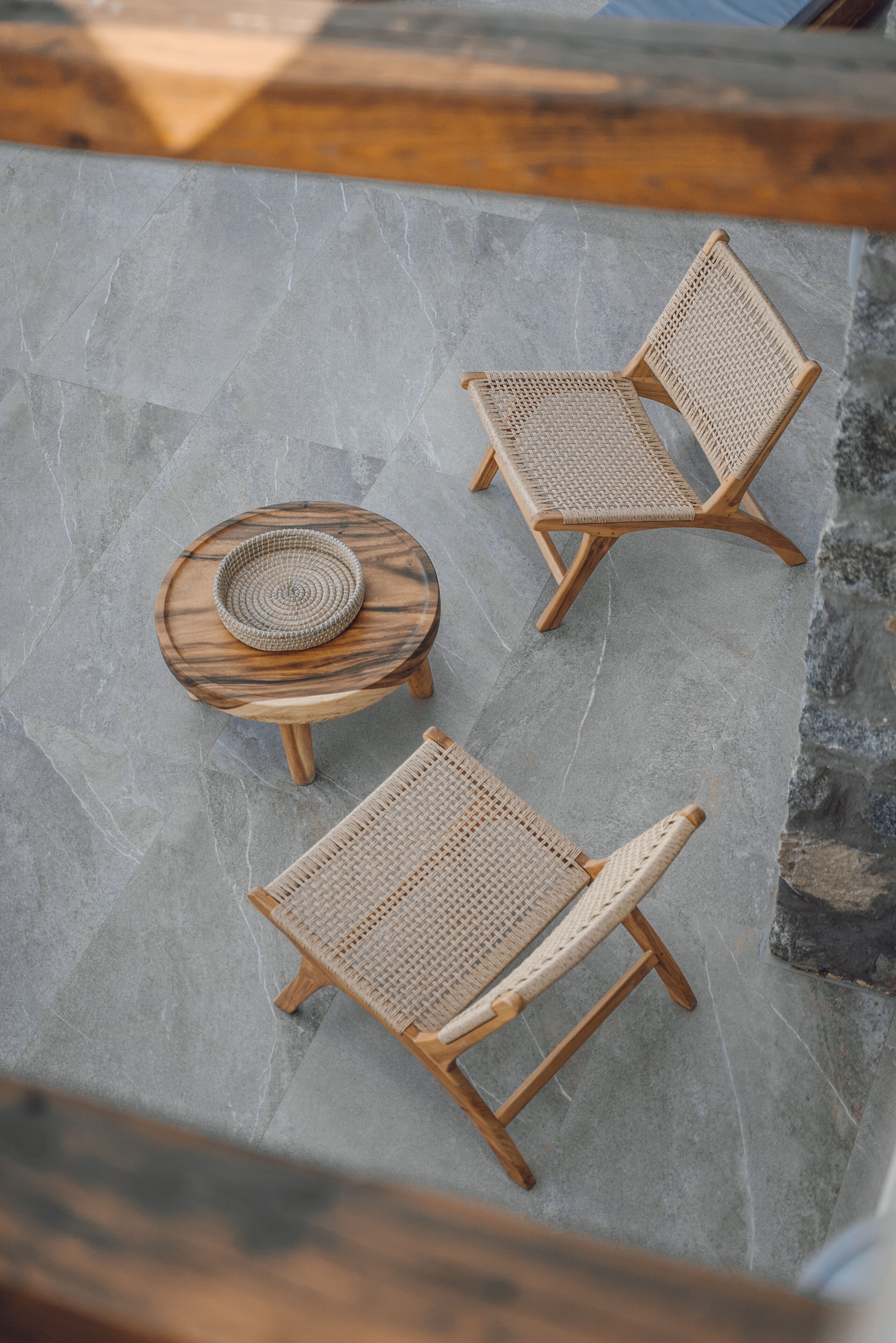 A set of three wicker lounge chairs and a small wooden table with a woven centerpiece on a stone patio.