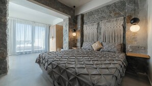 Een slaapkamer met een stenen muur, een bed met een bedspreide met een geometrisch patroon, een macramé wanddecoratie en een hanglamp.