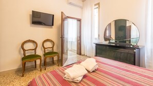 A hotel room with a bed, two chairs, a TV, a dresser, and a mirror. - Dolcevita Apartments N. 496 (Venice)
