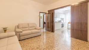 A spacious living area with a beige sofa, a glass coffee table, and a kitchen visible through an open door. - Dolcevita Apartments N. 496 (Venice)