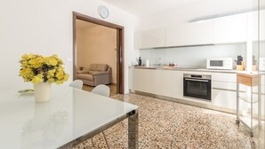 A modern kitchen with white cabinets, a microwave, and a small oven. There is a dining table with a vase of yellow flowers. - Dolcevita Apartments N. 496 (Venice)