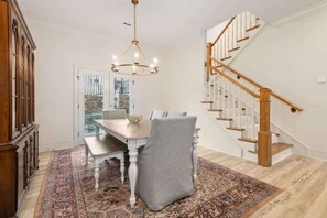 Ein Essbereich mit Tisch und Stühlen, einer Kristallleuchter, einer Treppe und einem gemusterten Teppich.