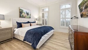 A bedroom with a bed, a nightstand, a dresser, a ceiling fan, and a window with shutters.
