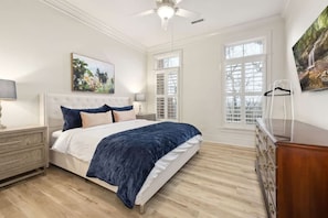 Un dormitorio con cama, mesita de noche, cómoda, ventilador de techo y ventana con persianas.