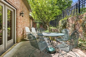 Eine Terrasse mit rundem Tisch und Metallstühlen, einer Ziegelwand und einem schwarzen Metallzaun.