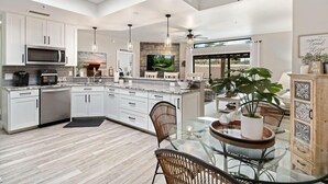 Une cuisine moderne avec des meubles blancs, un grand îlot central et un coin repas comprenant une table et des chaises en verre.