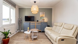 A living room with a sofa, a TV, a dining table, and a potted plant. - Ty Mamm, Petit Cocon Breton à 2 pas de la Plage (Plouescat)