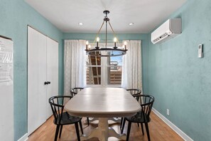 A dining room with a table, chairs, a chandelier, and an air conditioning unit. - 2 BD Condo I Steps From Lake Mich (Michigan City)