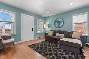 A living room with a sofa, a chair, a lamp, and a mirror. - 2 BD Condo I Steps From Lake Mich (Michigan City)