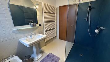 Et badeværelse med et håndvaskarrangement, et bidét, et toilet, et håndklædestativ, en bruser og et spejl.
