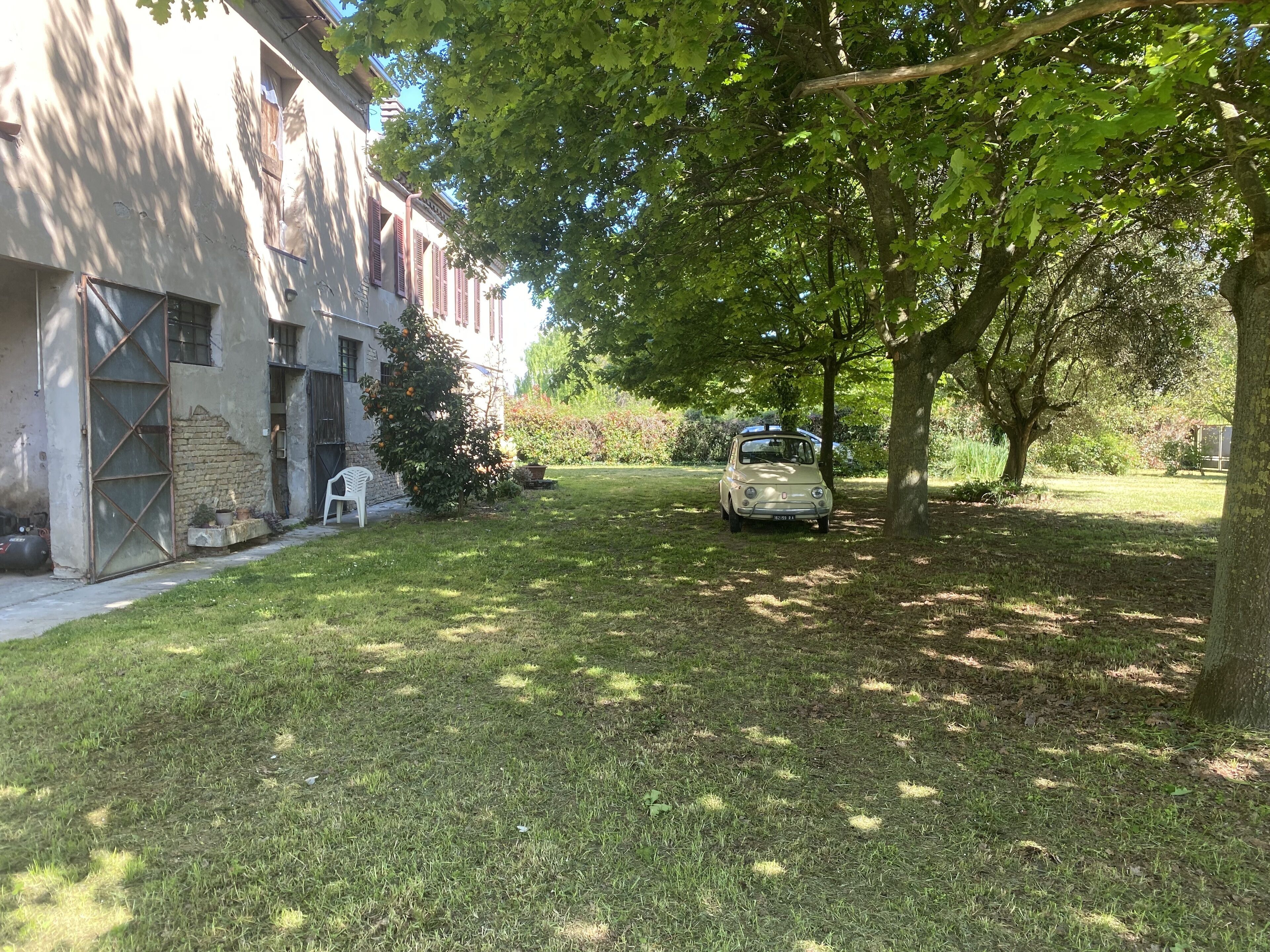 A courtyard with a parked car, a building with a brick facade, and a tree providing shade.