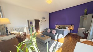 A modern living room with a sofa, coffee table, and a dining area. There is a bed with a headboard and a dresser with a mirror. - Family room Fico's colors (San Lorenzo)