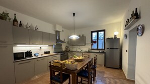 A modern kitchen with a dining table, chairs, and various kitchen appliances. - Family room Fico's colors (San Lorenzo)