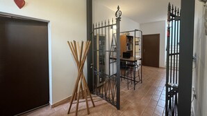 Ein Flur mit Holztür, einem Metallgitter, einem Holzständer und einem Schreibtisch mit einem Laptop.